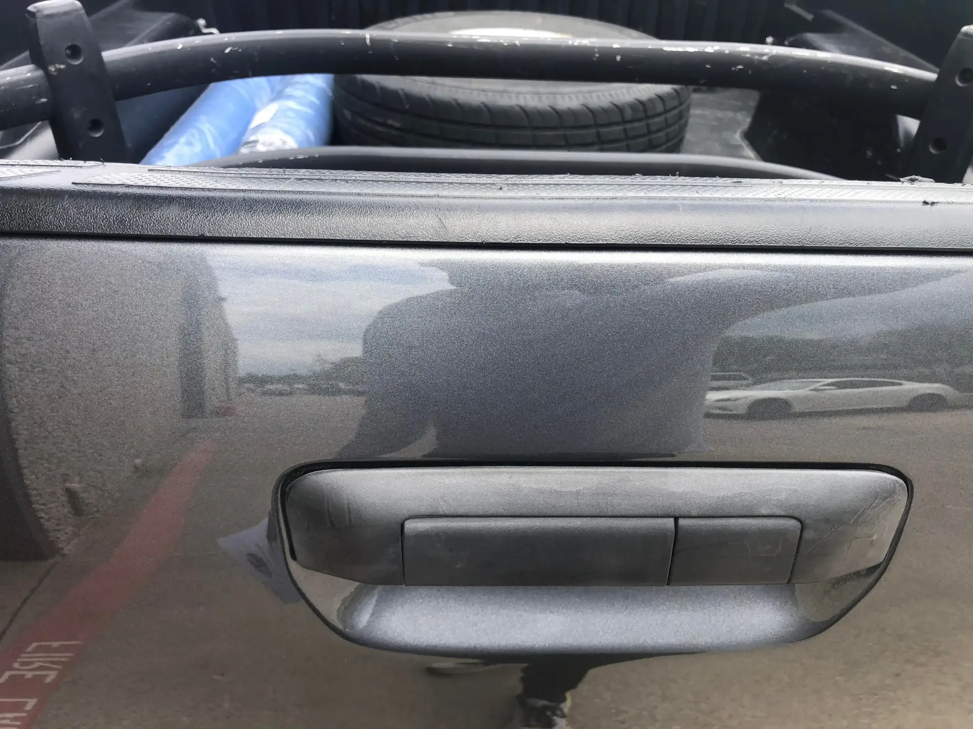 A close-up view of a dark gray pickup truck tailgate, featuring the handle and a spare tire in the truck bed.