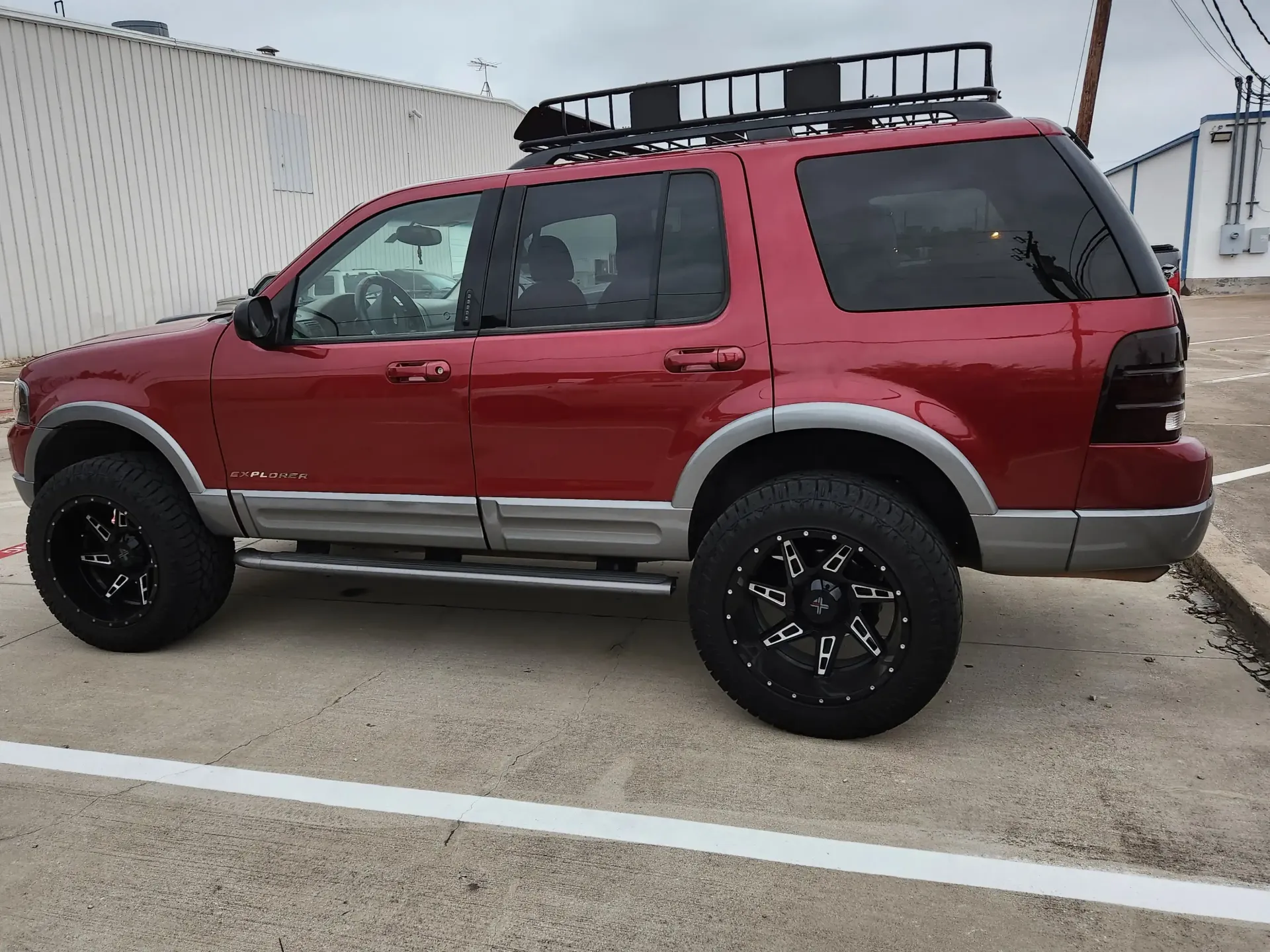 A lifted red Ford Explorer SUV with black rims and a roof cargo rack parked in a paved lot.