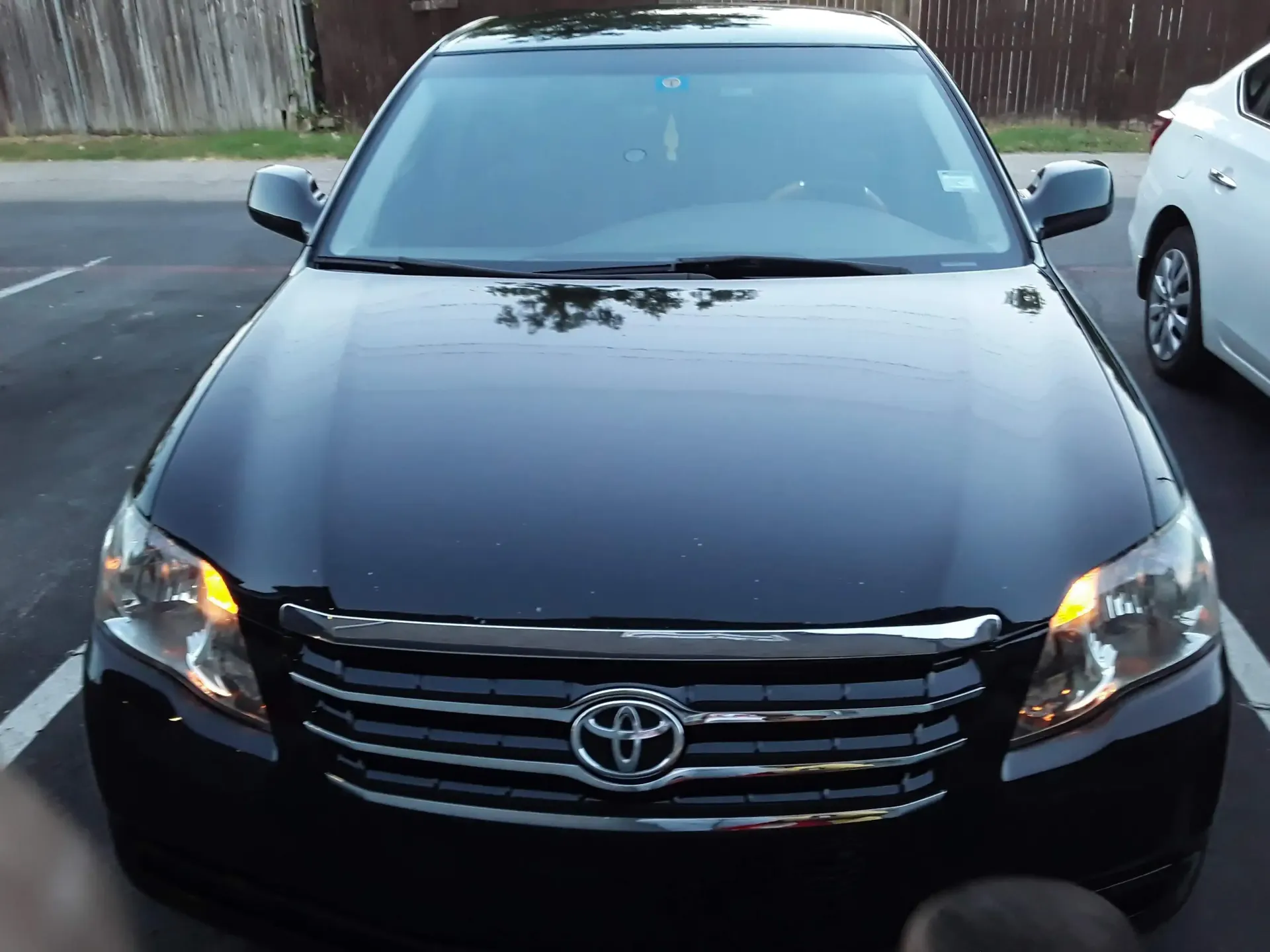 A front-view, eye-level shot of a parked black Toyota Avalon with its parking lights on.
