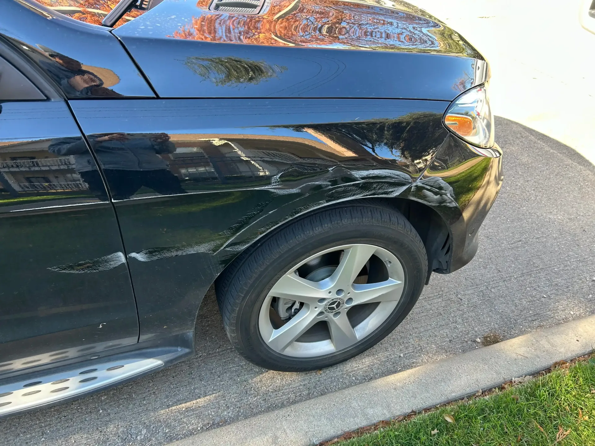 A black vehicle with significant paint damage and scratches along the front passenger-side fender and wheel arch.