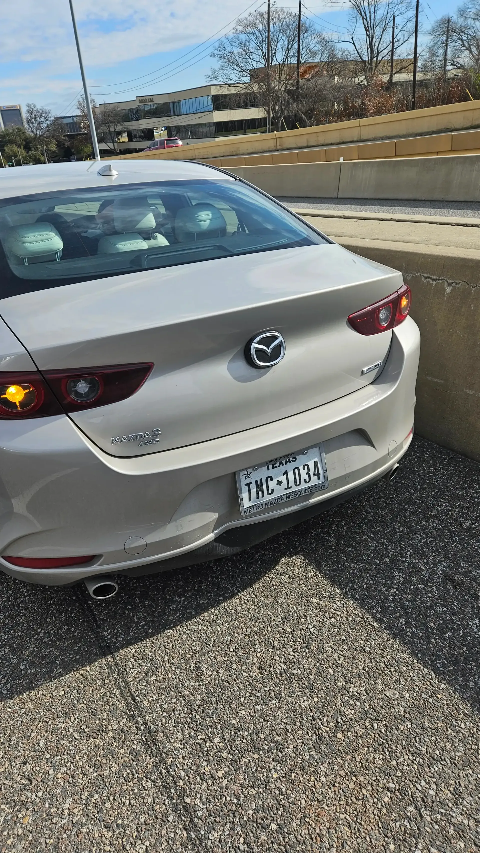 A silver Mazda sedan parked on a gravel surface next to a concrete wall.