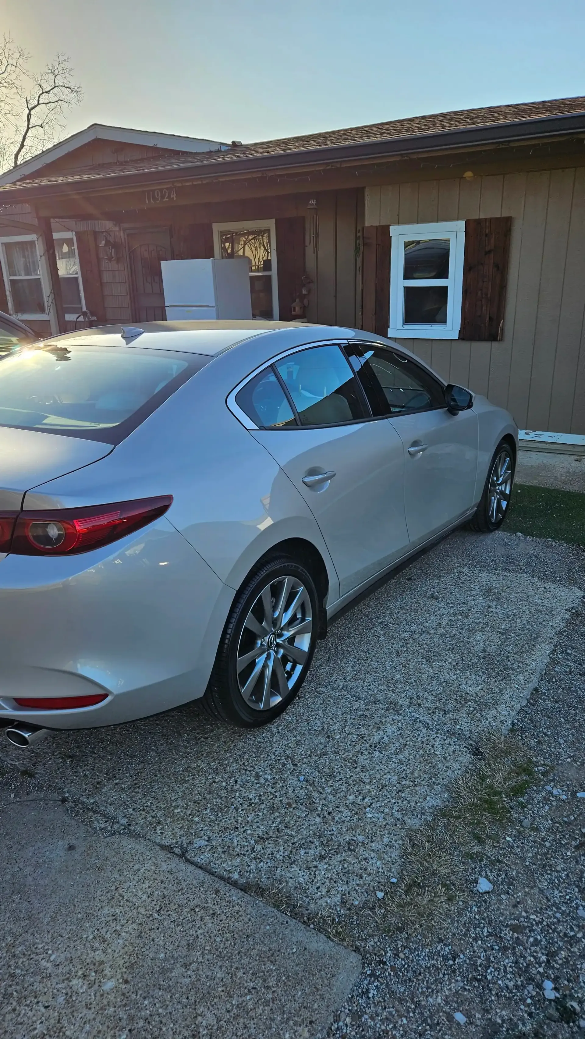 A silver sedan parked on a gravel driveway in front of a house on a sunny day.