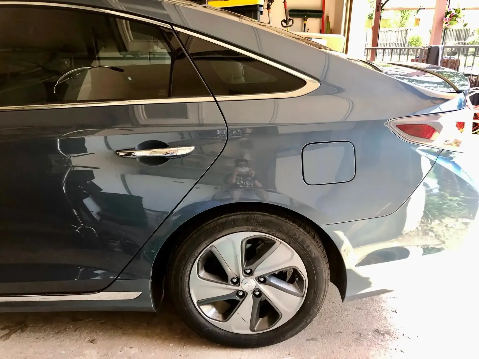 A close-up side view of a metallic blue sedan, showing the rear passenger door, alloy wheel, and fuel cap.