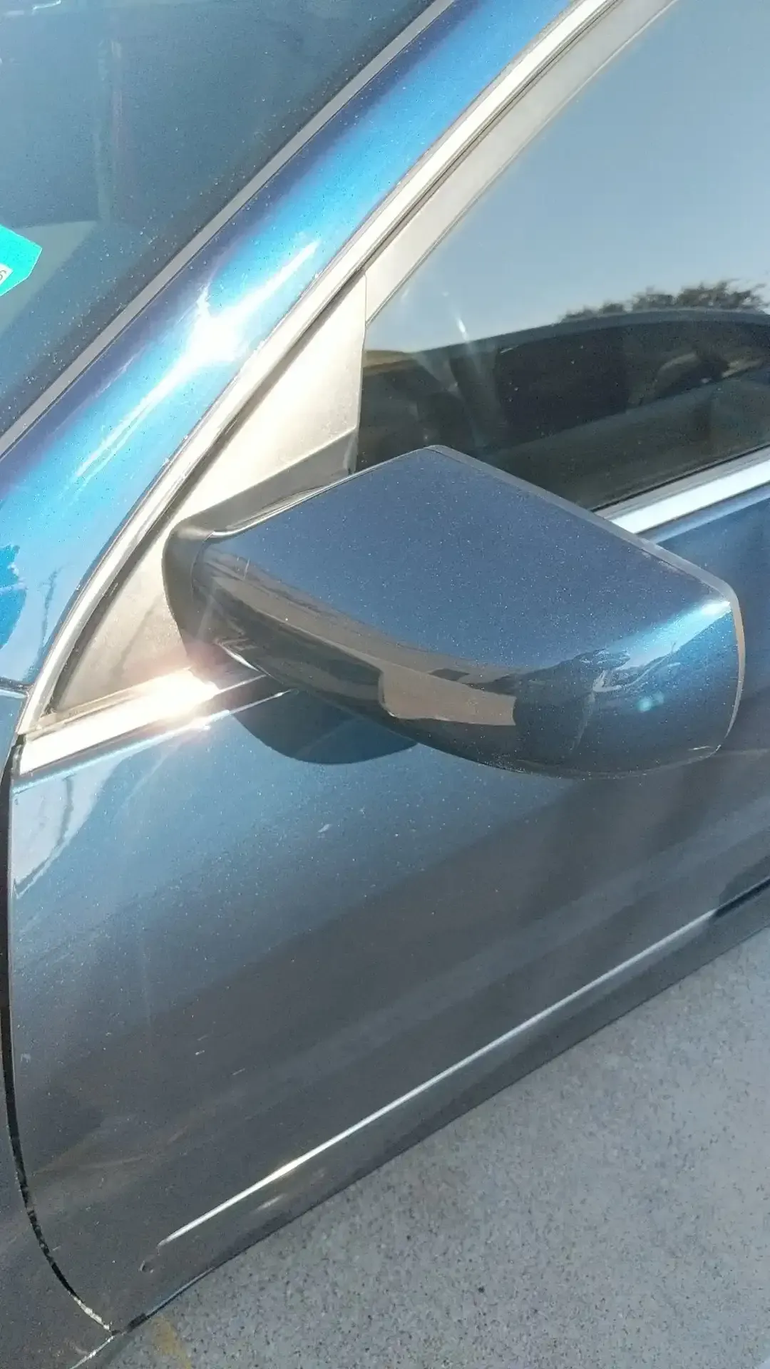 A dark blue car’s side-view mirror attached to the driver's side door, reflecting part of the window frame and exterior.