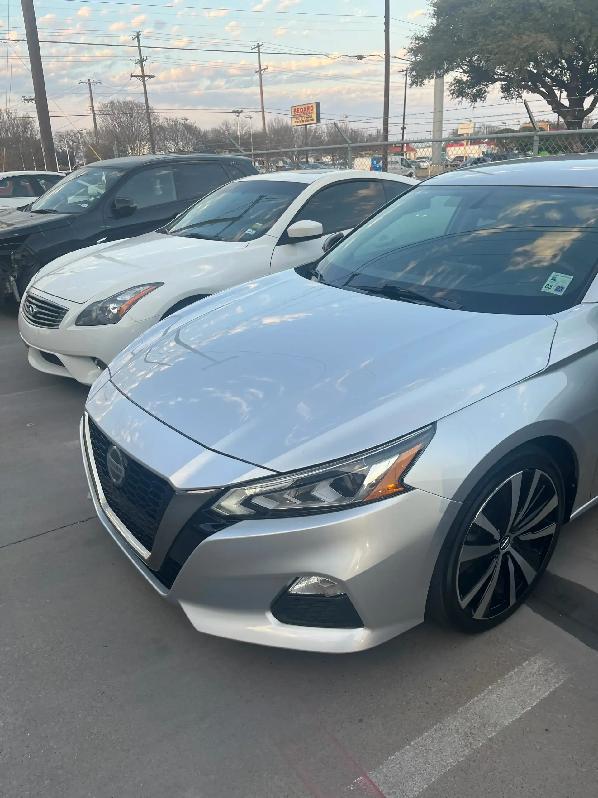 A silver Nissan Altima parked in a car lot with a white sedan behind it.