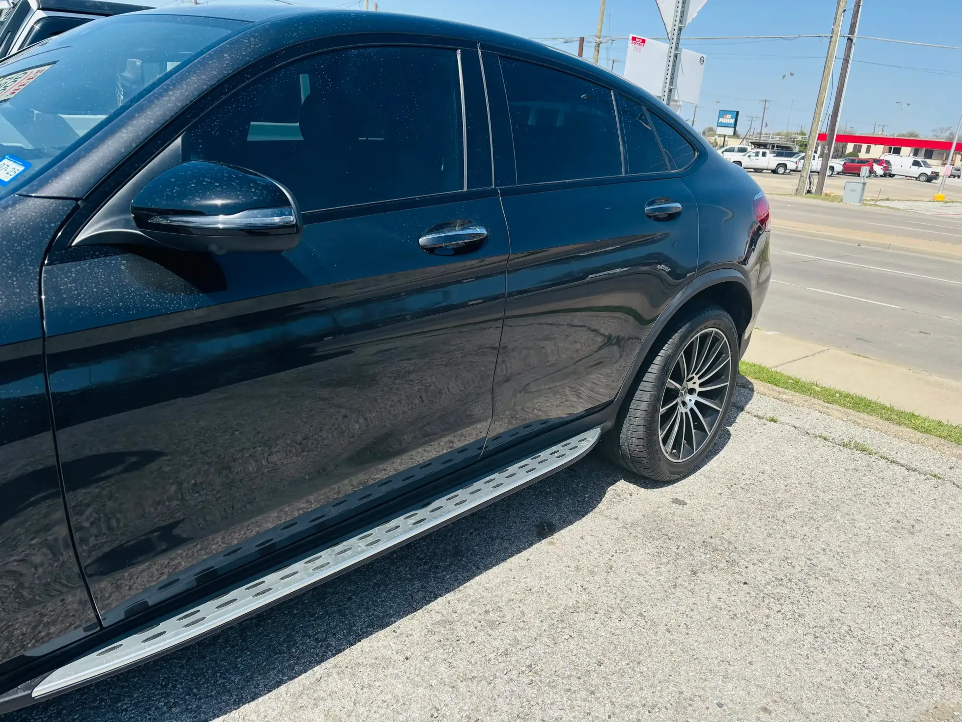 A side view of a black SUV with tinted windows and custom wheels parked on a gravel lot near a street.