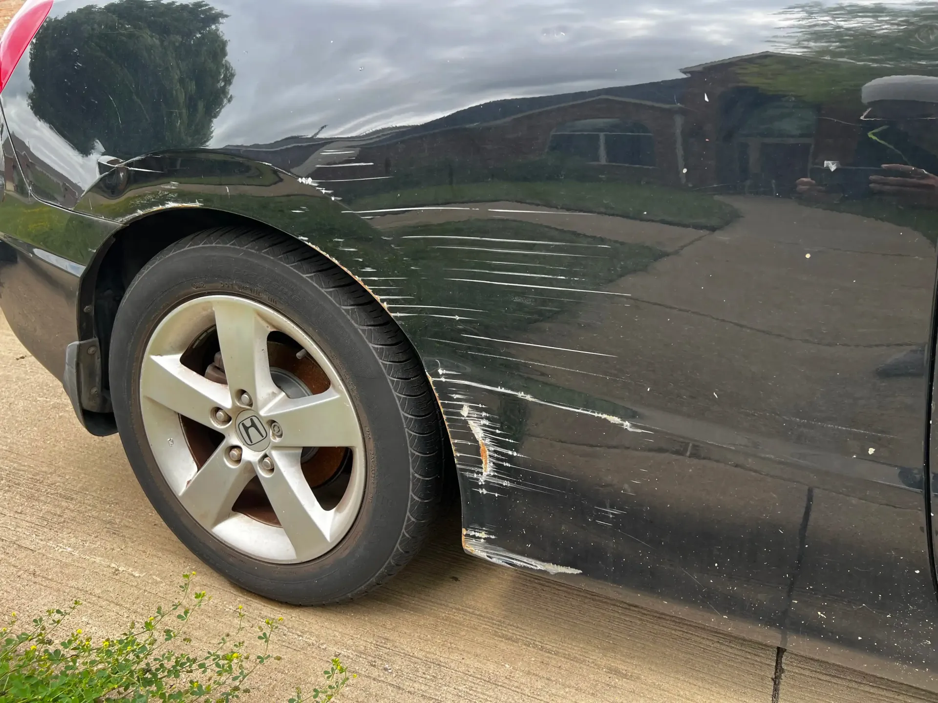 Black car rear fender showing paint scuffs, scratches, and damage along the wheel well and side panel.