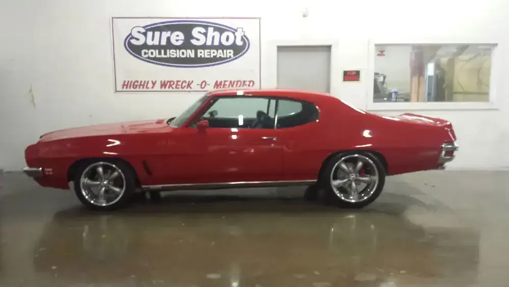 A red vintage Pontiac GTO coupe parked inside a collision repair shop.