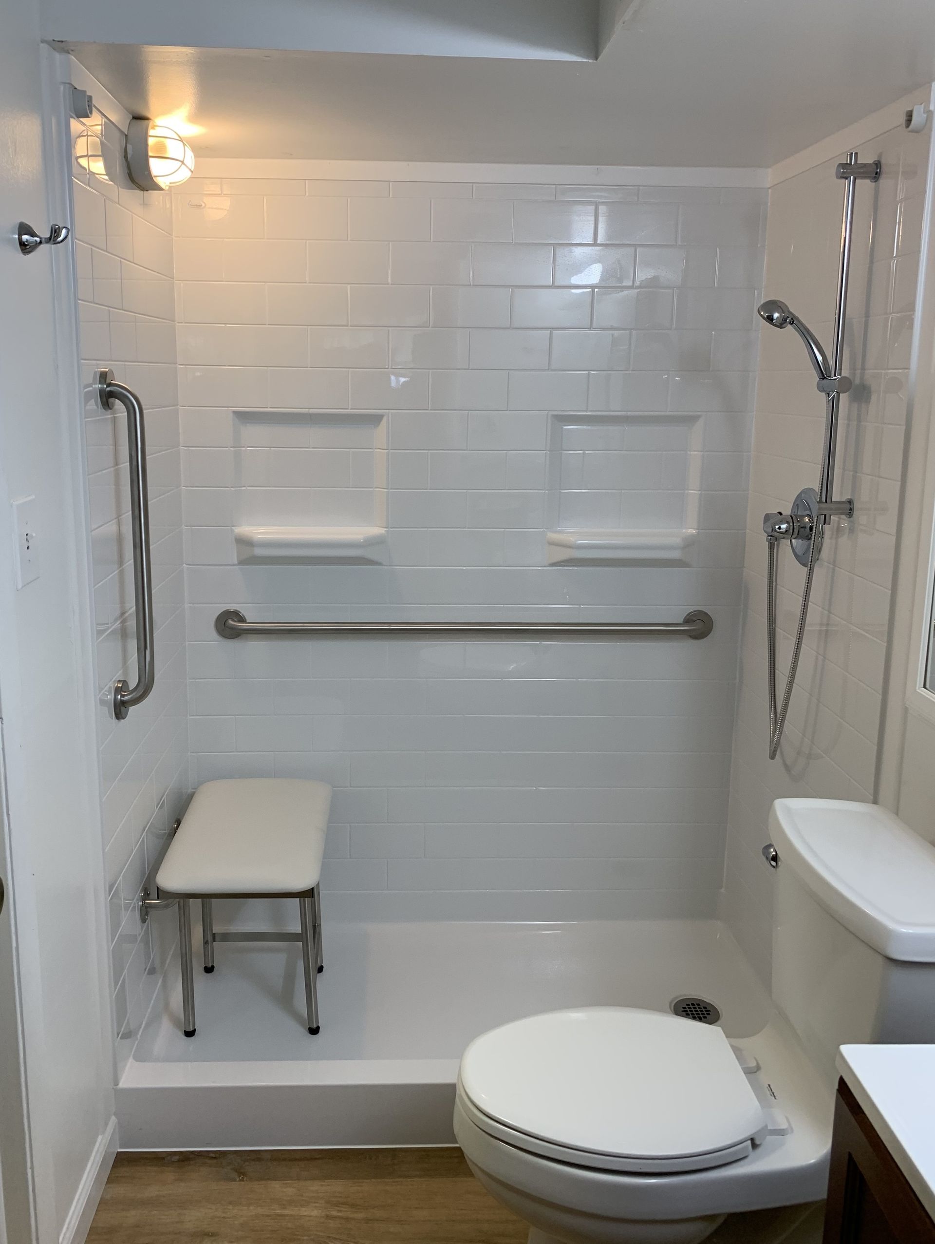 Accessible bathroom with walk-in shower, grab bars, fold-down seat, and raised toilet.