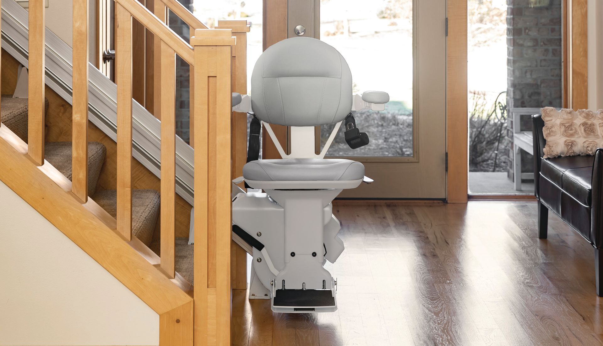 Small white robot vacuum in a wooden-floored hallway near a staircase and front door.