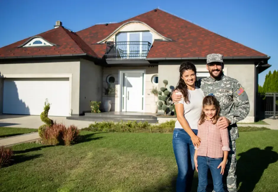 Family of three standing in front of their home; man in uniform, woman, and child, smiling.
