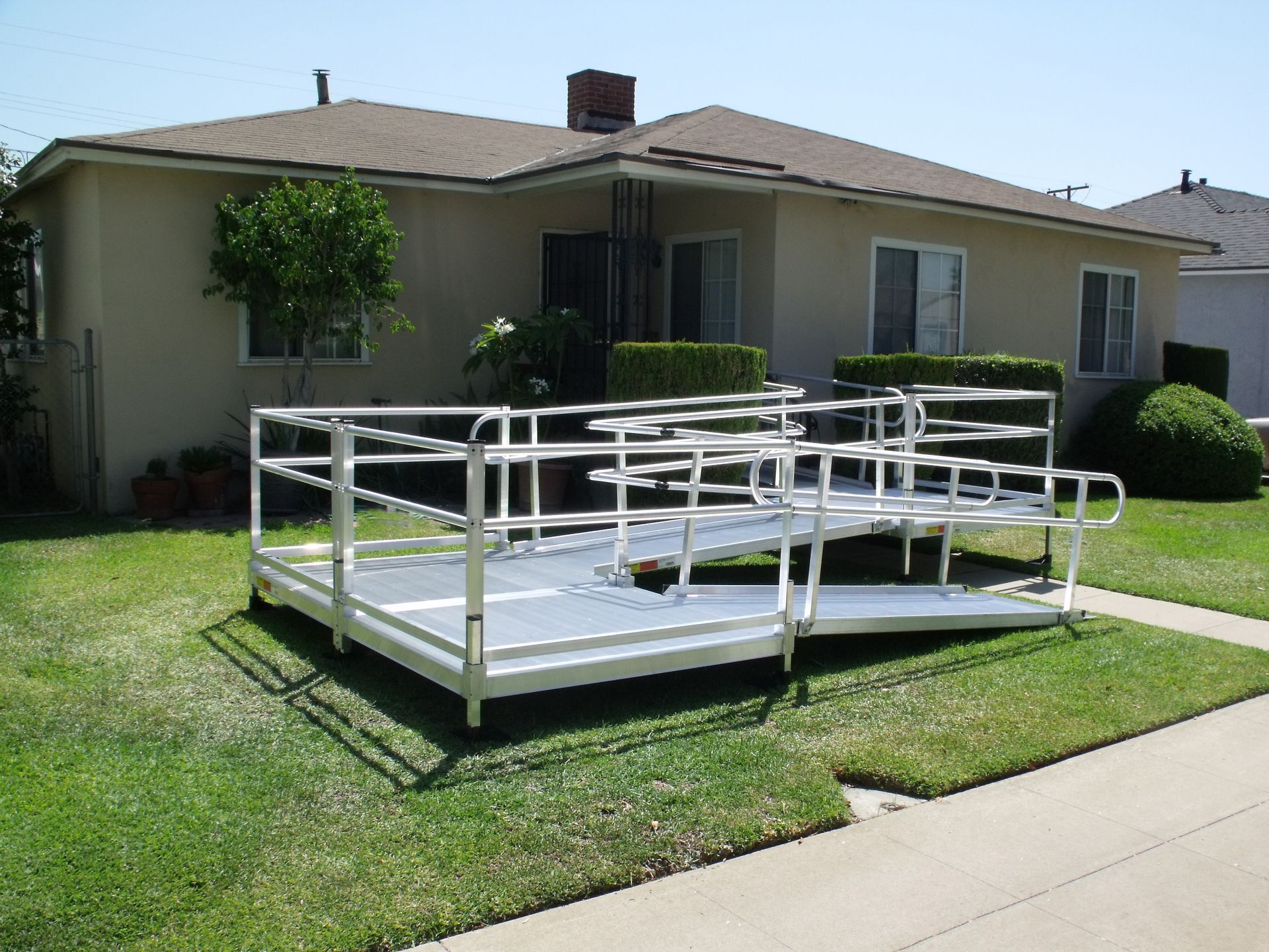 Long modular wheelchair ramp system with handrails spanning a home's front yard