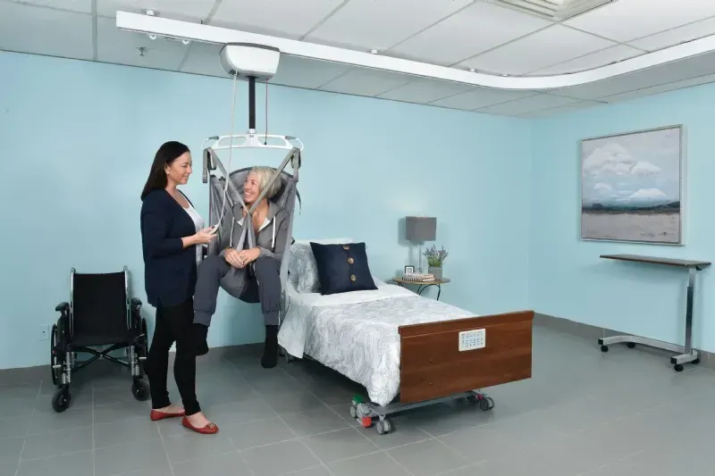 A caregiver helping an elderly woman in a hospital bed using a patient lift installed by Altamira Ltd.