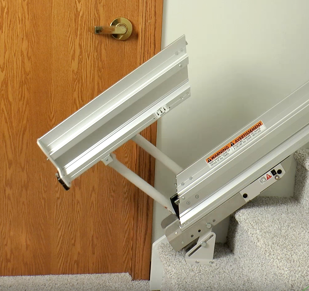 A Bruno stairlift sitting on the stairs in a living room next to a couch, installed by Altamira Ltd.
