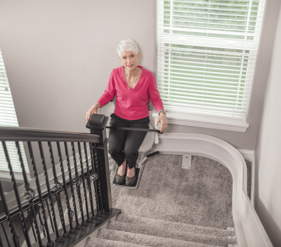An elderly woman is sitting on a curved bruno stair lift installed by Altamira Ltd.