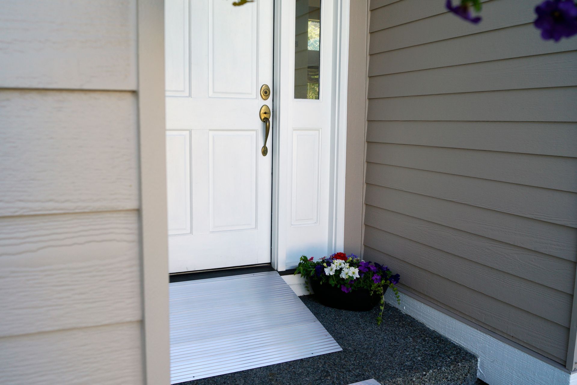 The front door of a house with an accessibility ramp and flowers on the porch