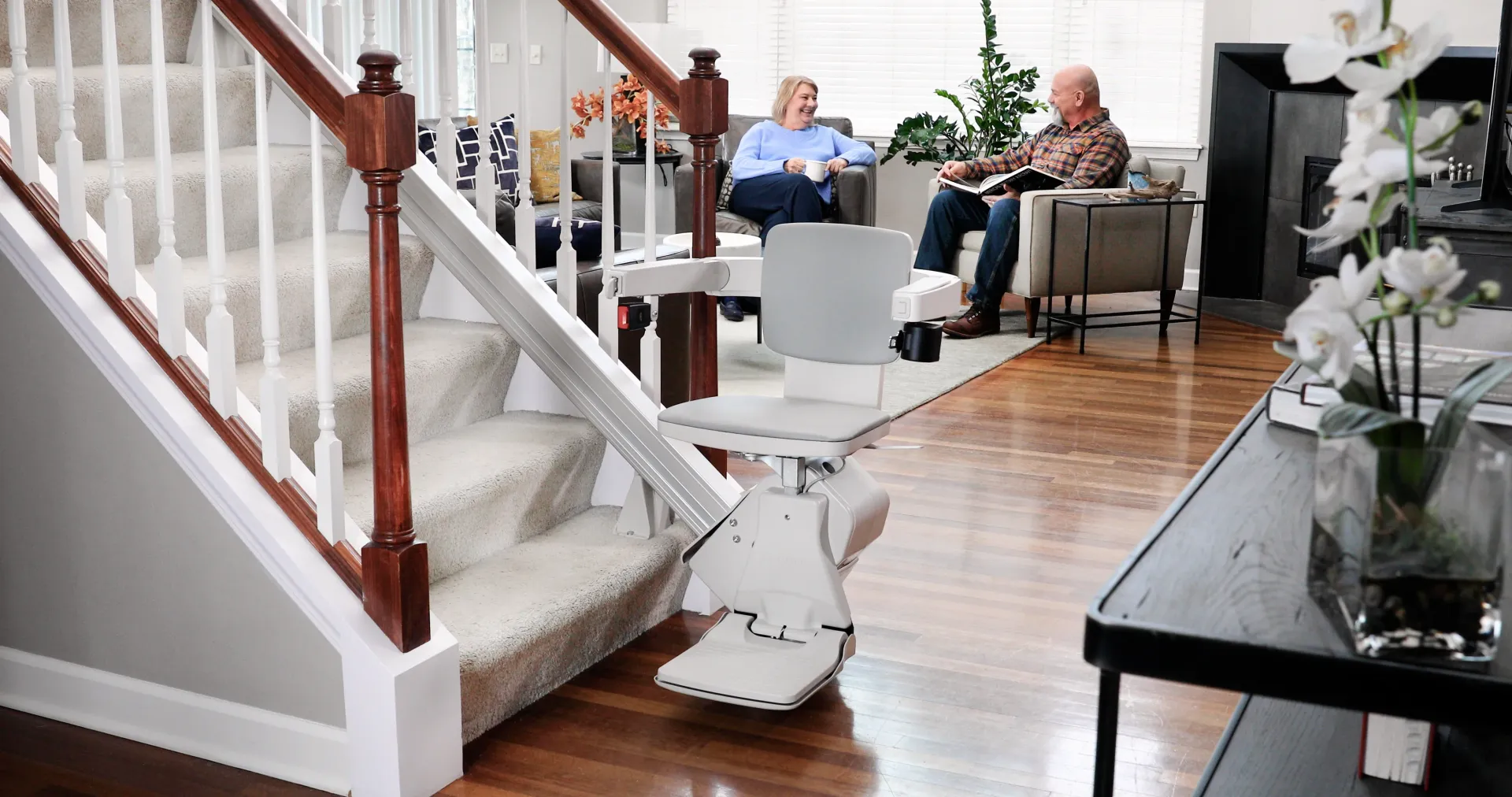 A Bruno Elan stairlift at the bottom of a staircase with a couple in the background.