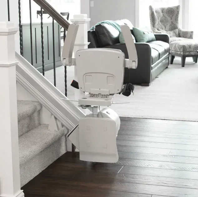 A Bruno Elan stairlift folded up in a living room next to a couch, installed by Altamira Ltd.