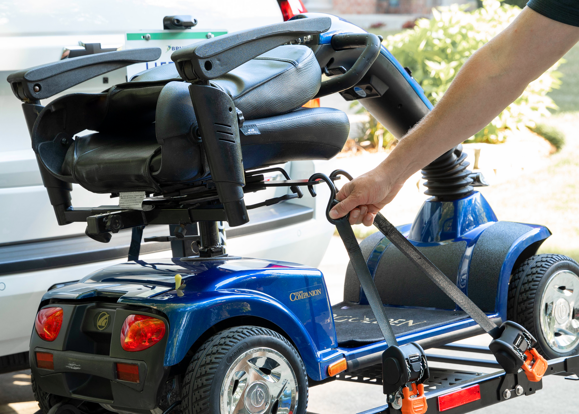 Blue mobility scooter being loaded into a vehicle lift by a person outdoors