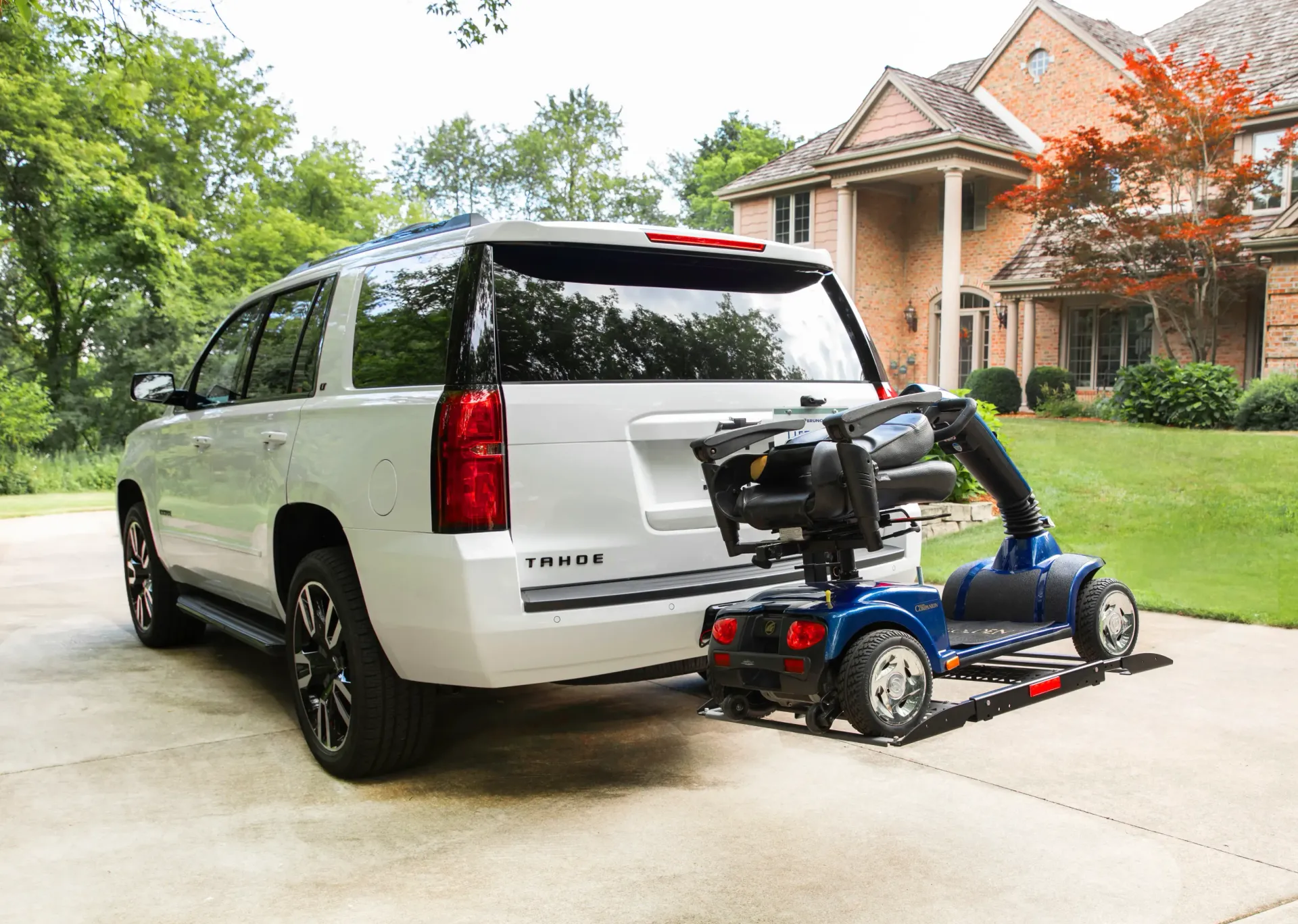 White SUV parked in a driveway with a blue mobility scooter lift attached at the rear