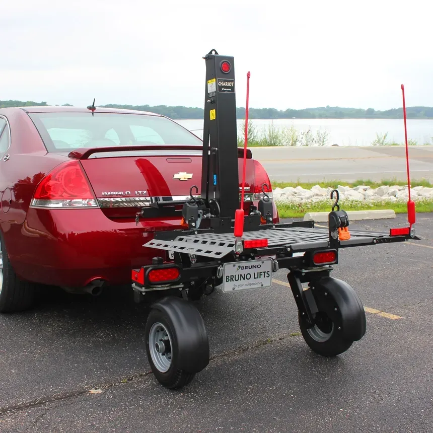 A Bruno Chariot trailer-style exterior vehicle lift towing a mobility device behind a car
