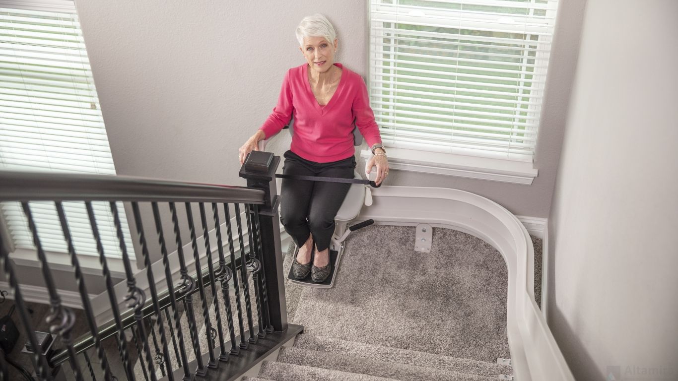 An elderly woman sitting on a curved indoor stair lift by Altamira Ltd. in New Jersey.