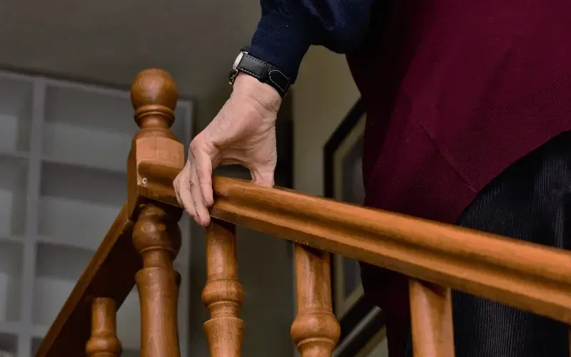 Person holding a stair railing with both hands while climbing stairs