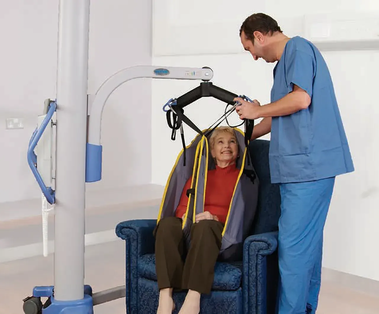 Caregiver using a Hoyer floor lift to transfer a woman in a sling into an armchair