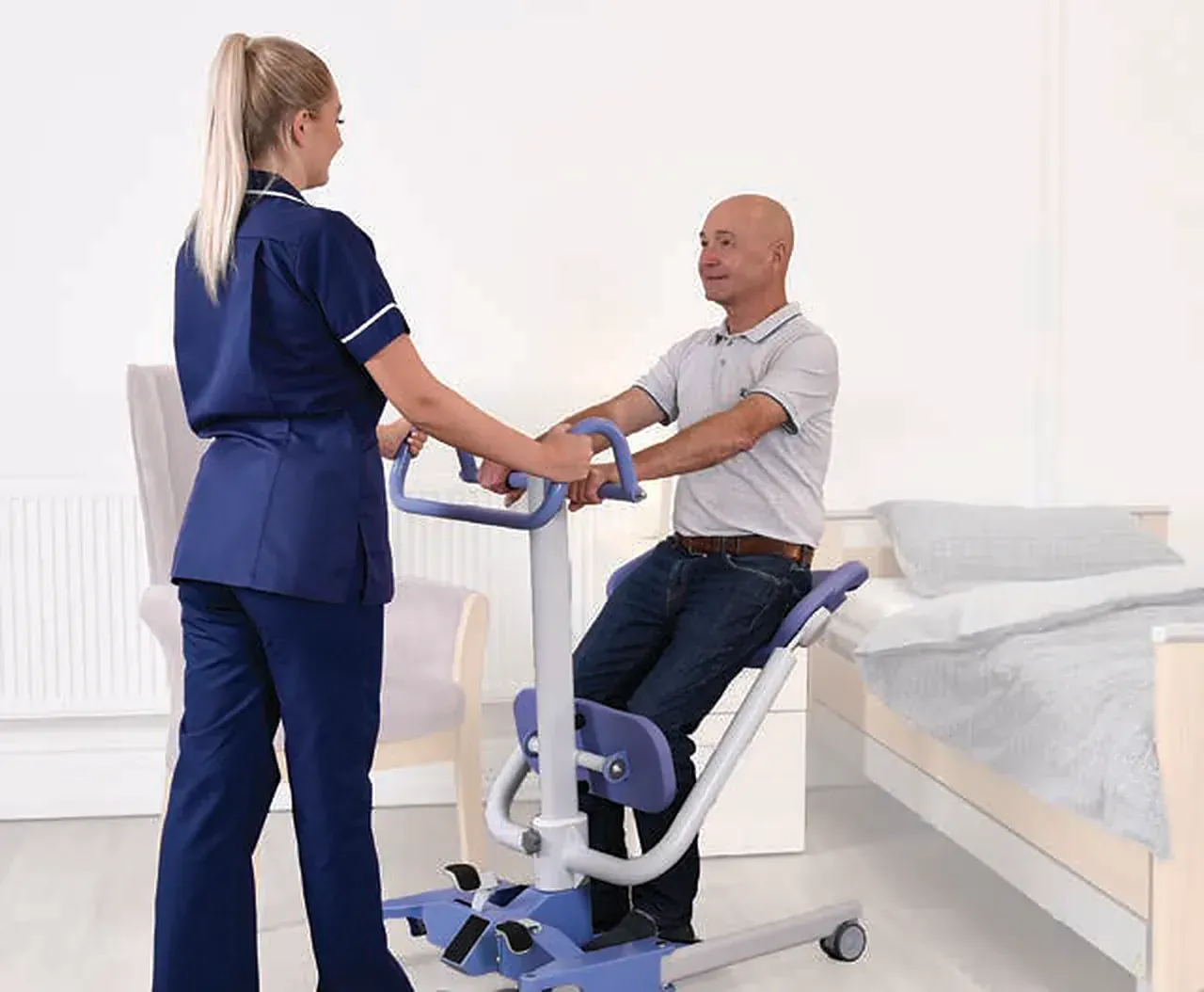 Caregiver helping a man stand using the Hoyer Up beside a bed