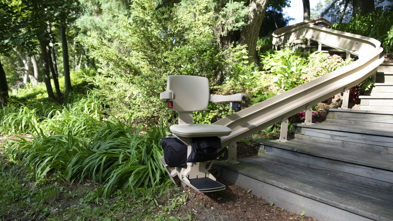An outdoor Bruno stair lift installed by Altamira Ltd. is sitting on the side of a wooden walkway.