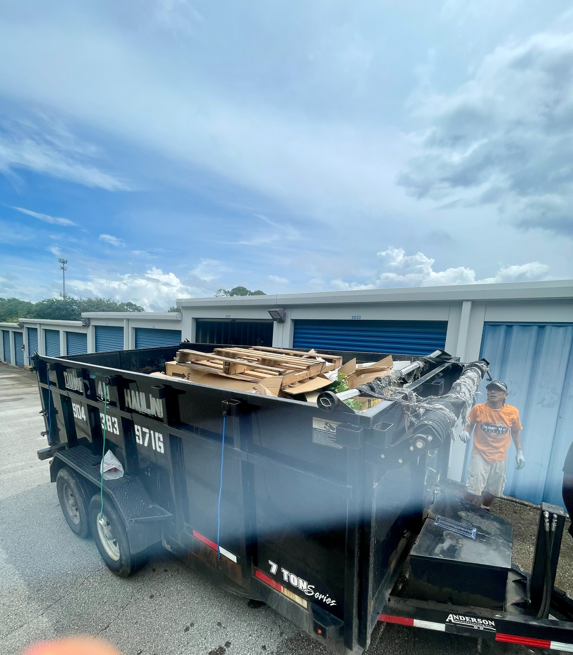Green dumpster filled with construction debris, in front of a brick building.