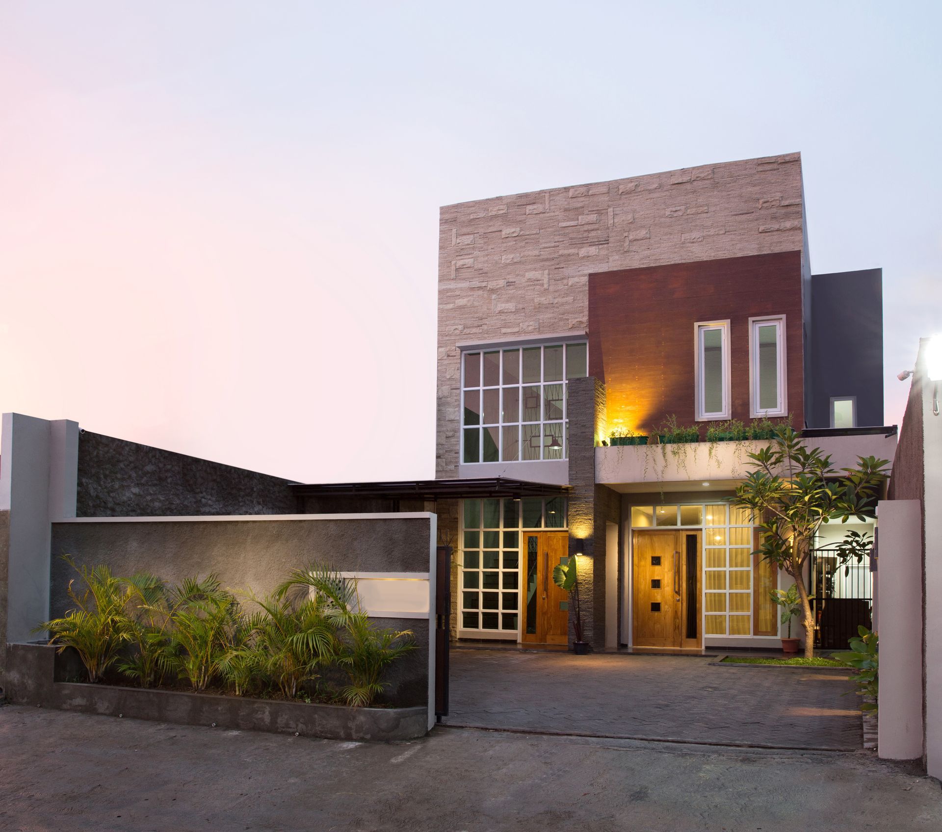 Modern two-story house with warm exterior lights and a driveway at dusk