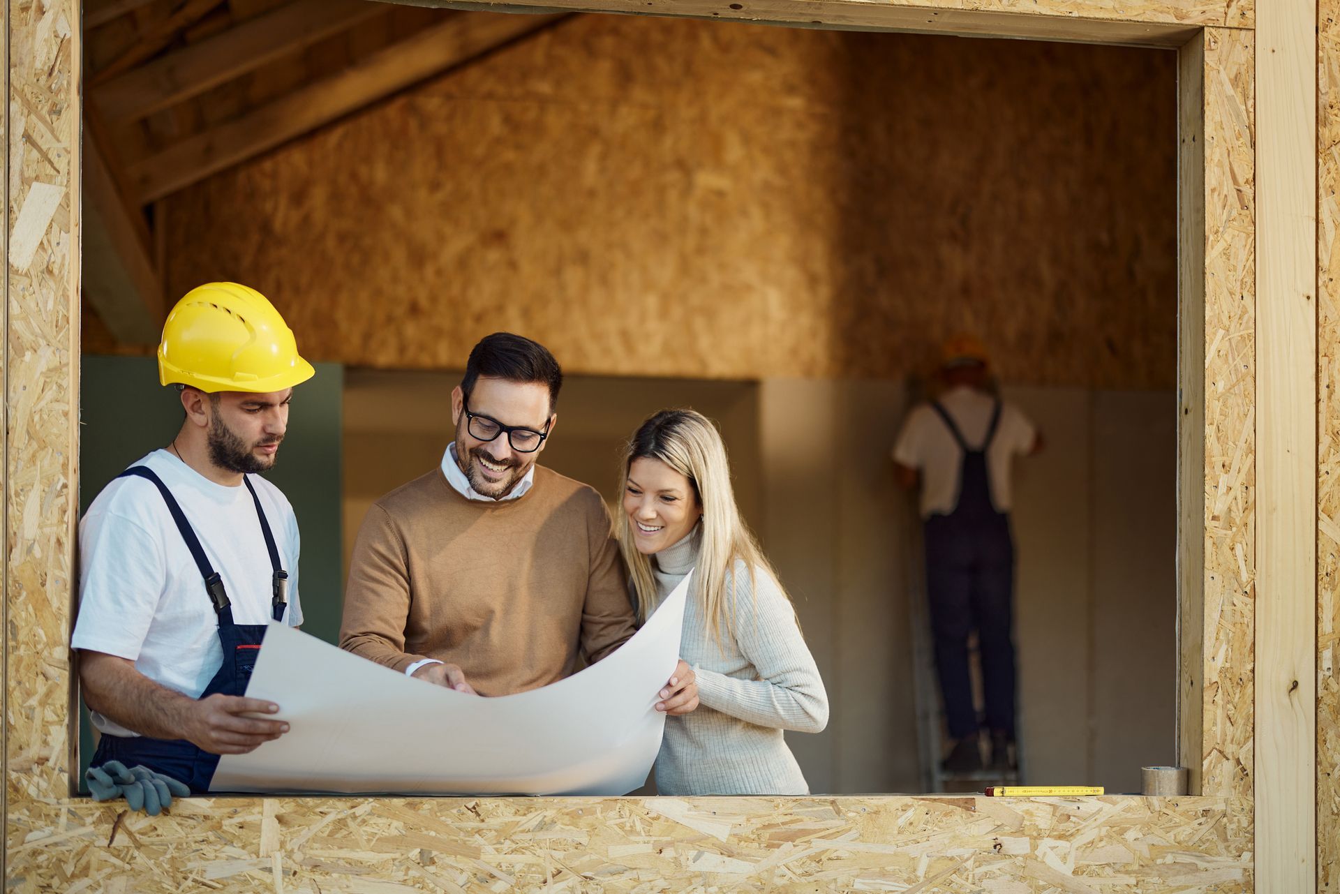 Happy couple analyzing blueprints with manual worker at construction site. Happy couple analyzing blueprints with manual worker at construction site.
