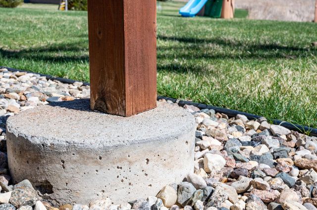 Wooden post set in a concrete base, surrounded by gravel and grass, in a yard.