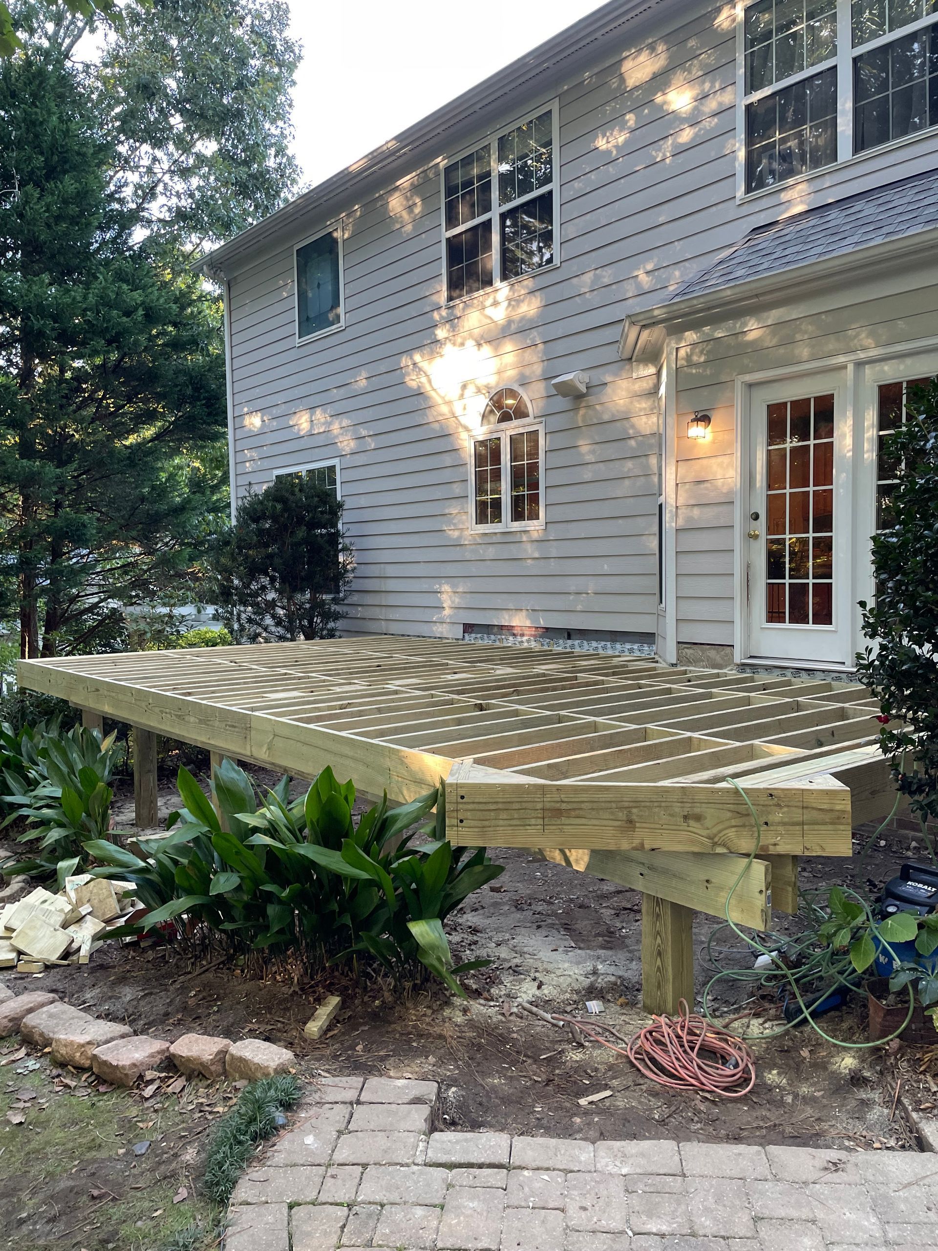 Newly constructed wooden deck attached to a two-story house, with sunlight dappling the surface.