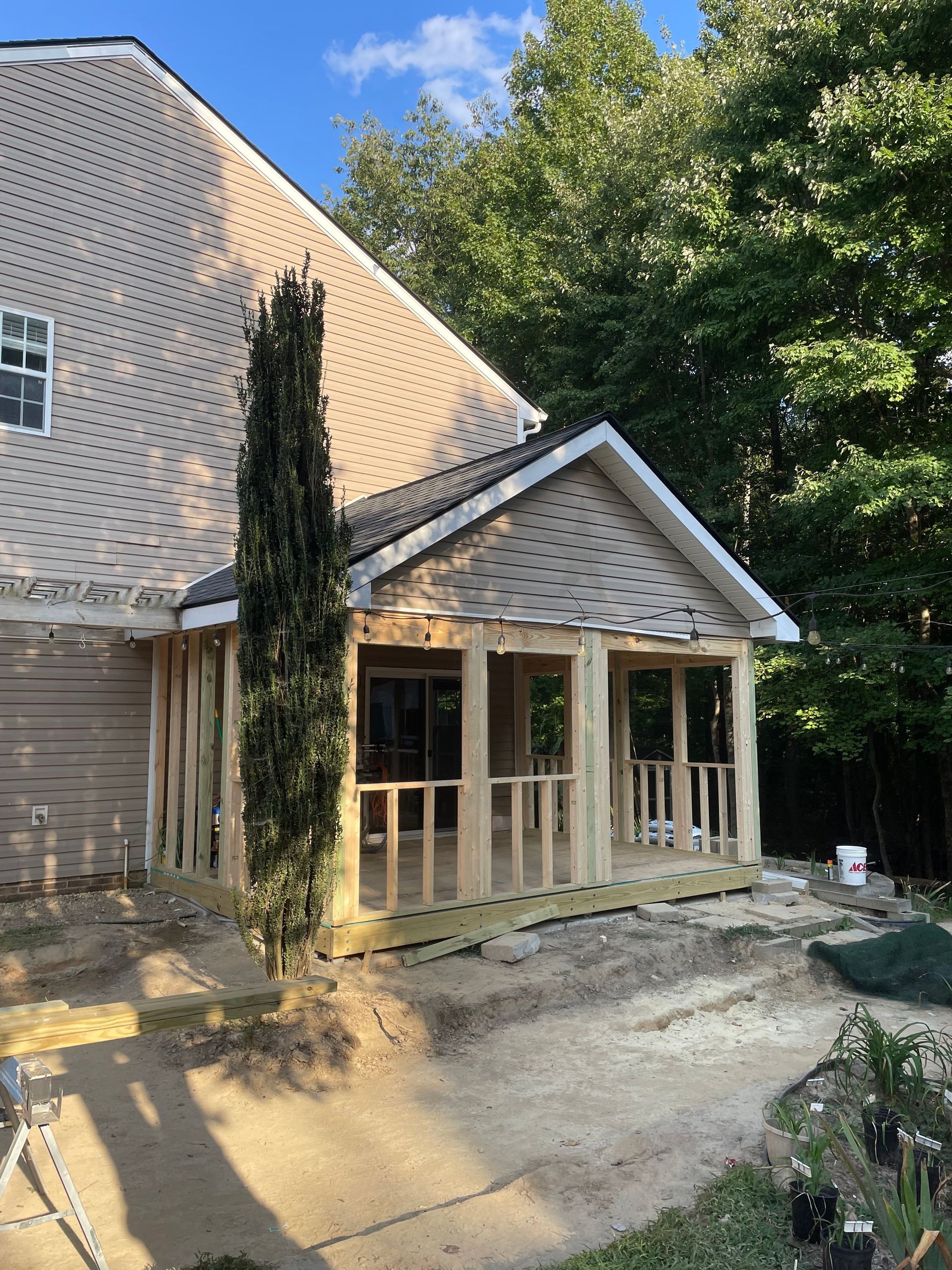 Construction of a porch addition attached to a house; unfinished wood framing and beige siding.