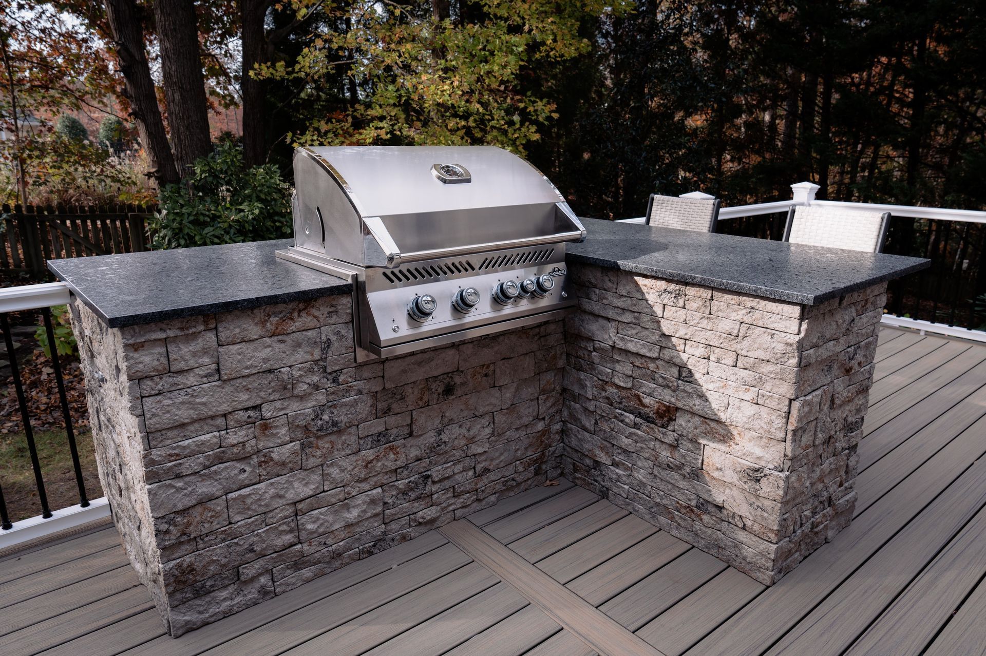 Outdoor kitchen with stainless steel grill and stone countertop on a deck.