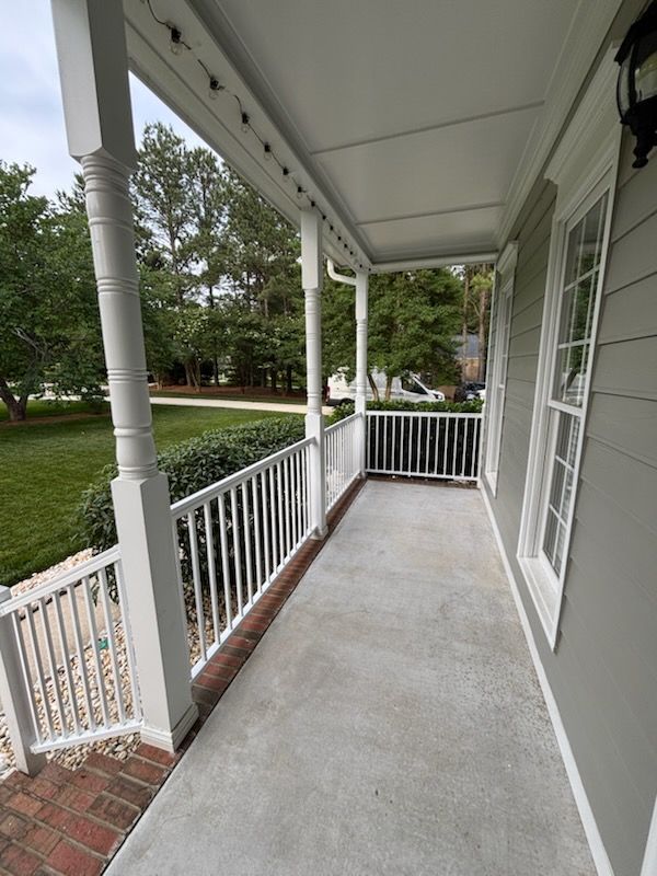 Covered porch with white railings, concrete floor, and view of a green yard and trees