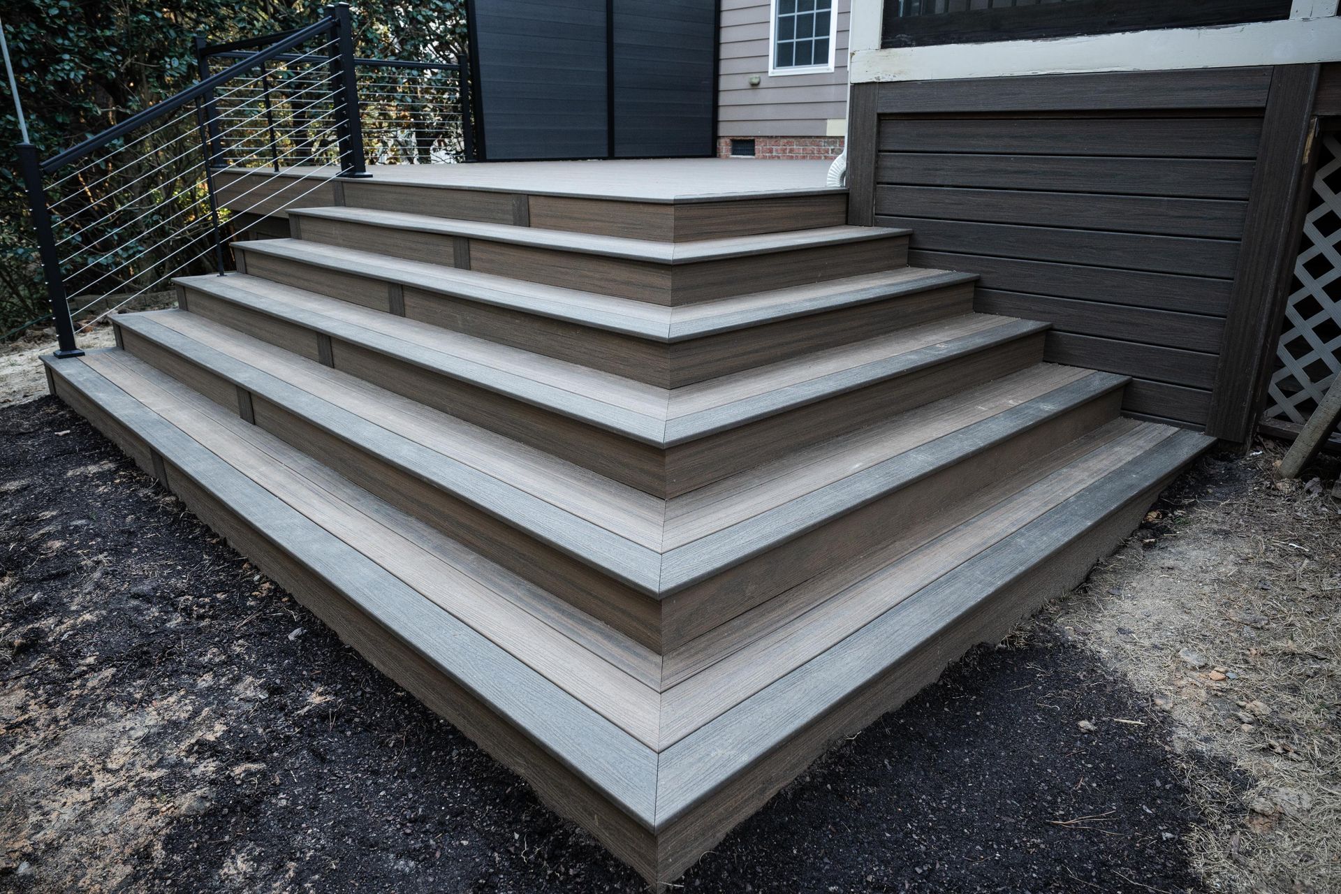 Wide, multi-tiered outdoor deck stairs with dark brown trim and light gray composite planks leading to a house entrance.