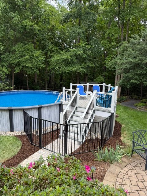 Above-ground pool with white stairs and blue railing in a wooded backyard