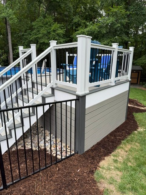 A newly constructed wooden deck featuring a railing alongside the side of a light-colored house with glass doors.
