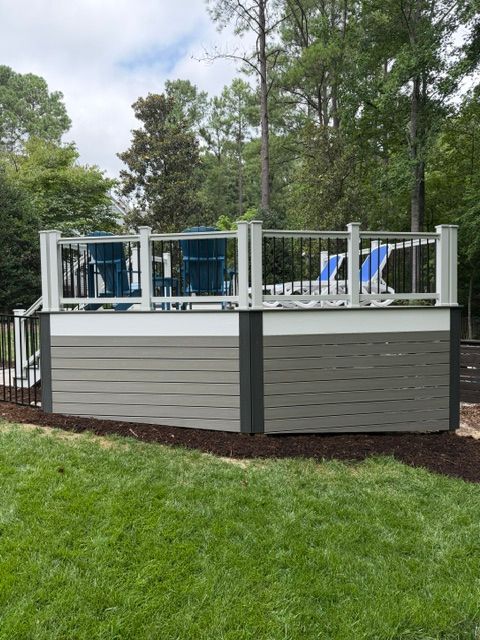 Raised outdoor deck with white railings and blue lounge chairs in a grassy backyard