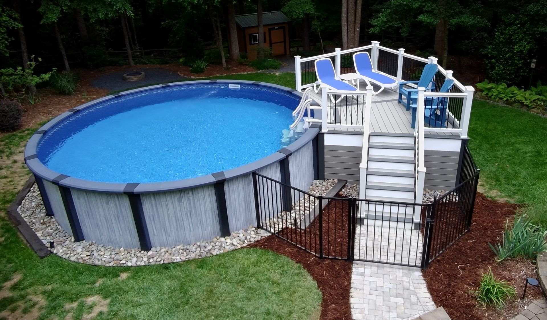 Above-ground backyard pool with deck and stairs, surrounded by grass and red mulch
