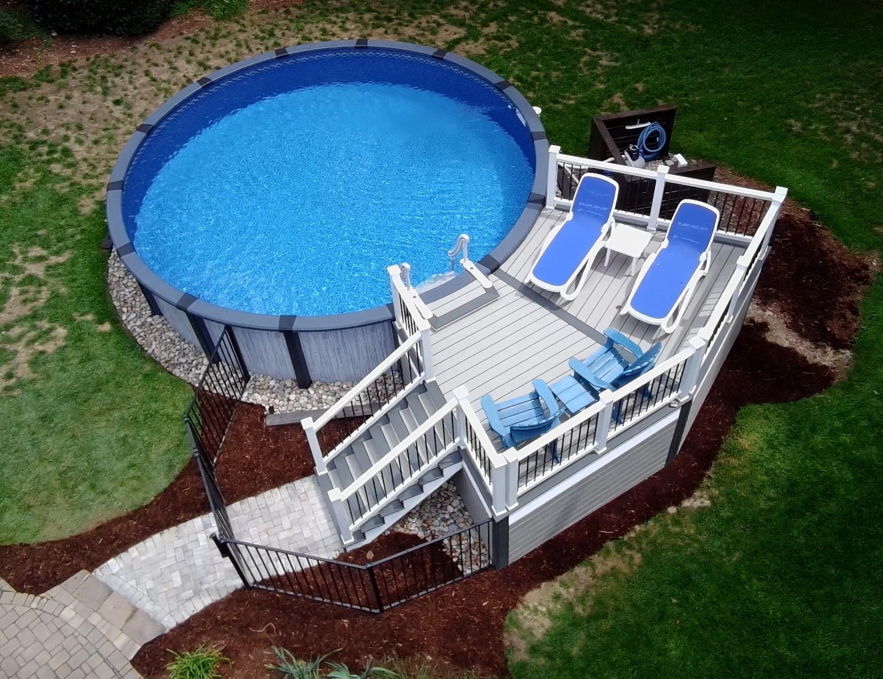 Above-ground pool with white deck, blue lounge chairs, and stairs in a backyard