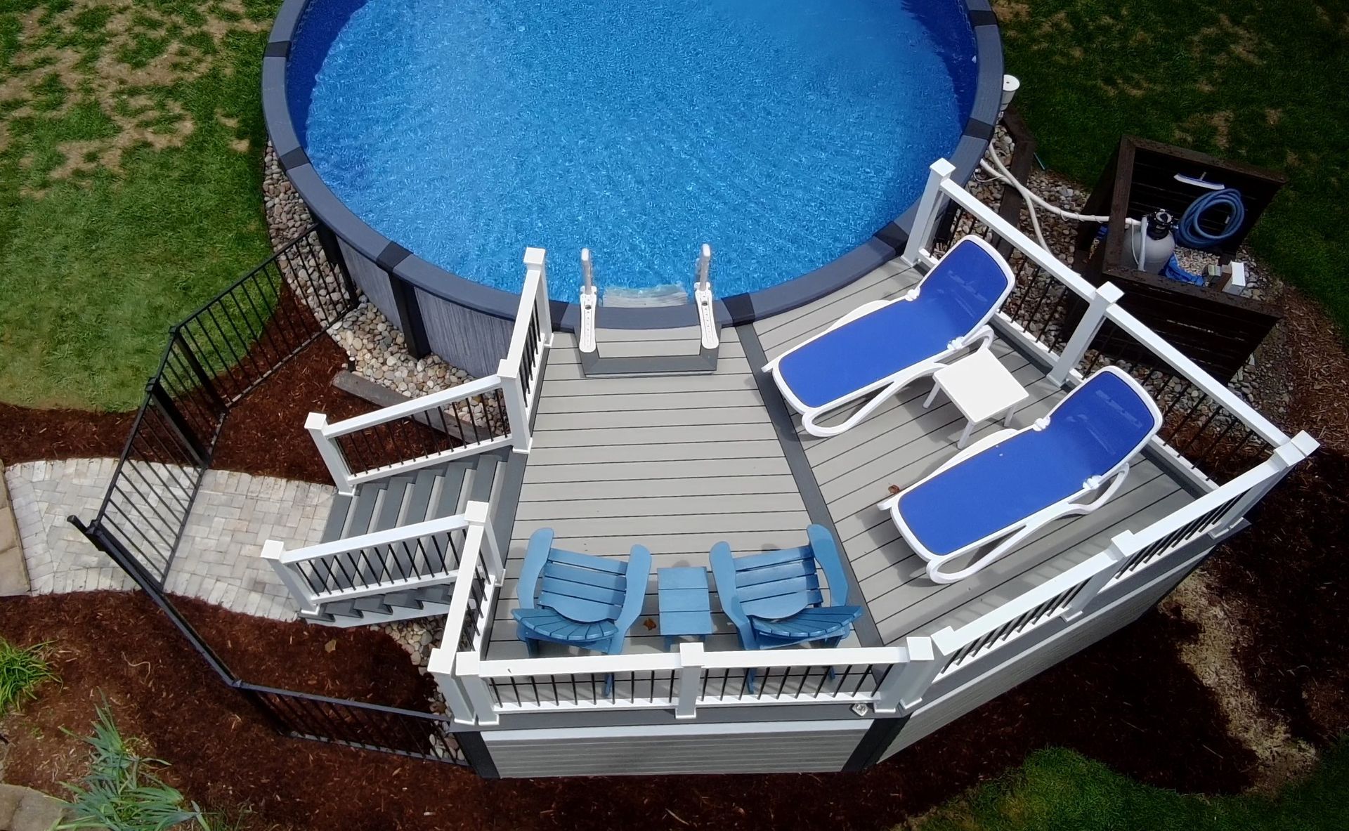 Backyard above-ground pool with gray deck and blue lounge chairs, viewed from above