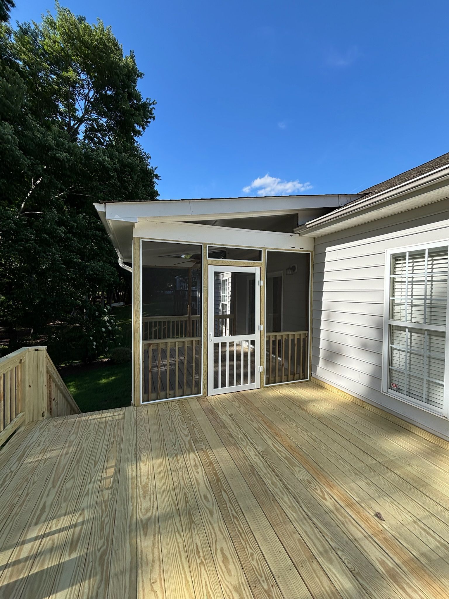 Exterior view of a cream-colored house with a newly constructed wooden deck and stairs leading to double glass doors.