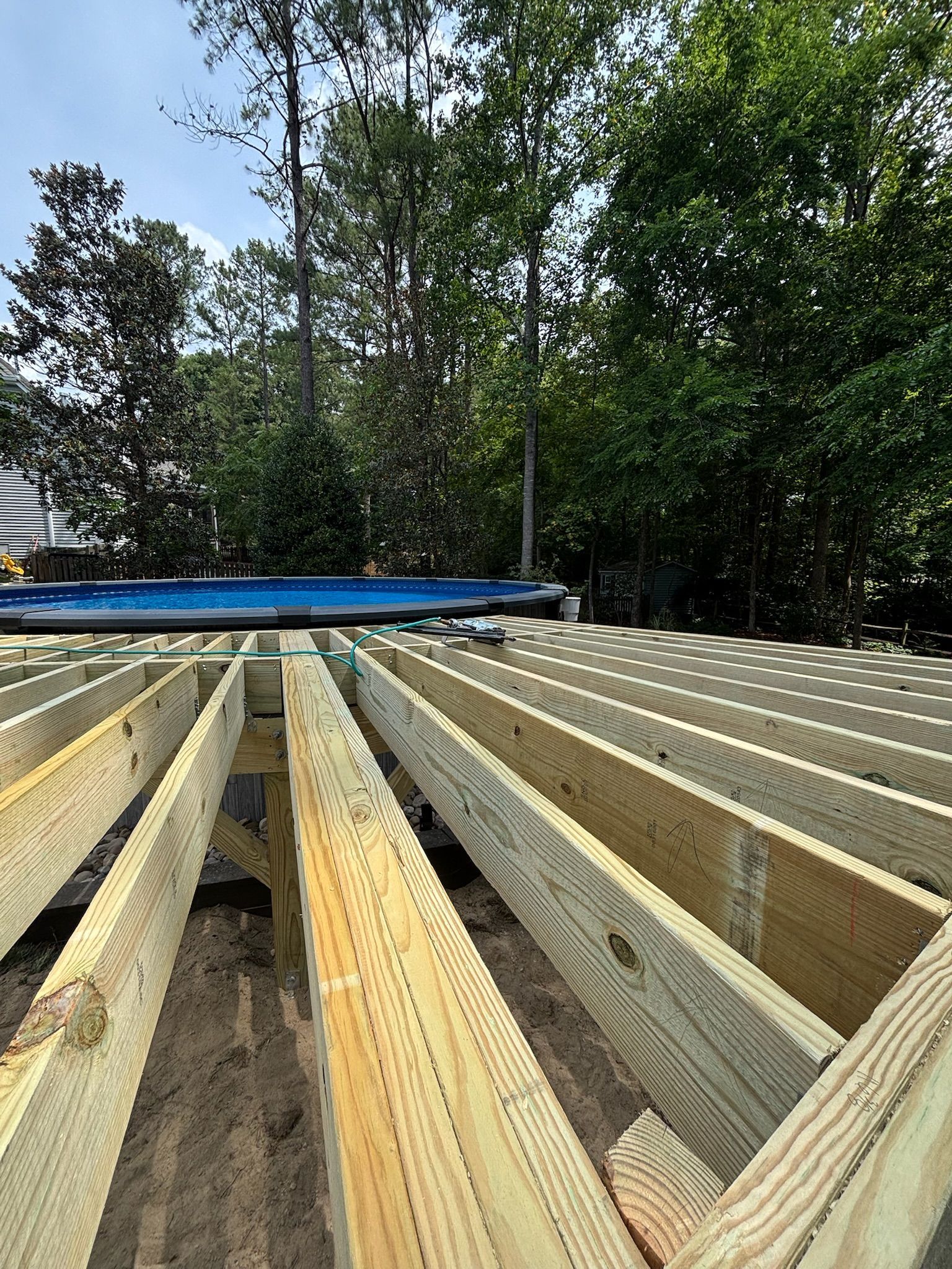 Wooden deck joists under construction with a blue beam, viewed from ground level outdoors against trees.