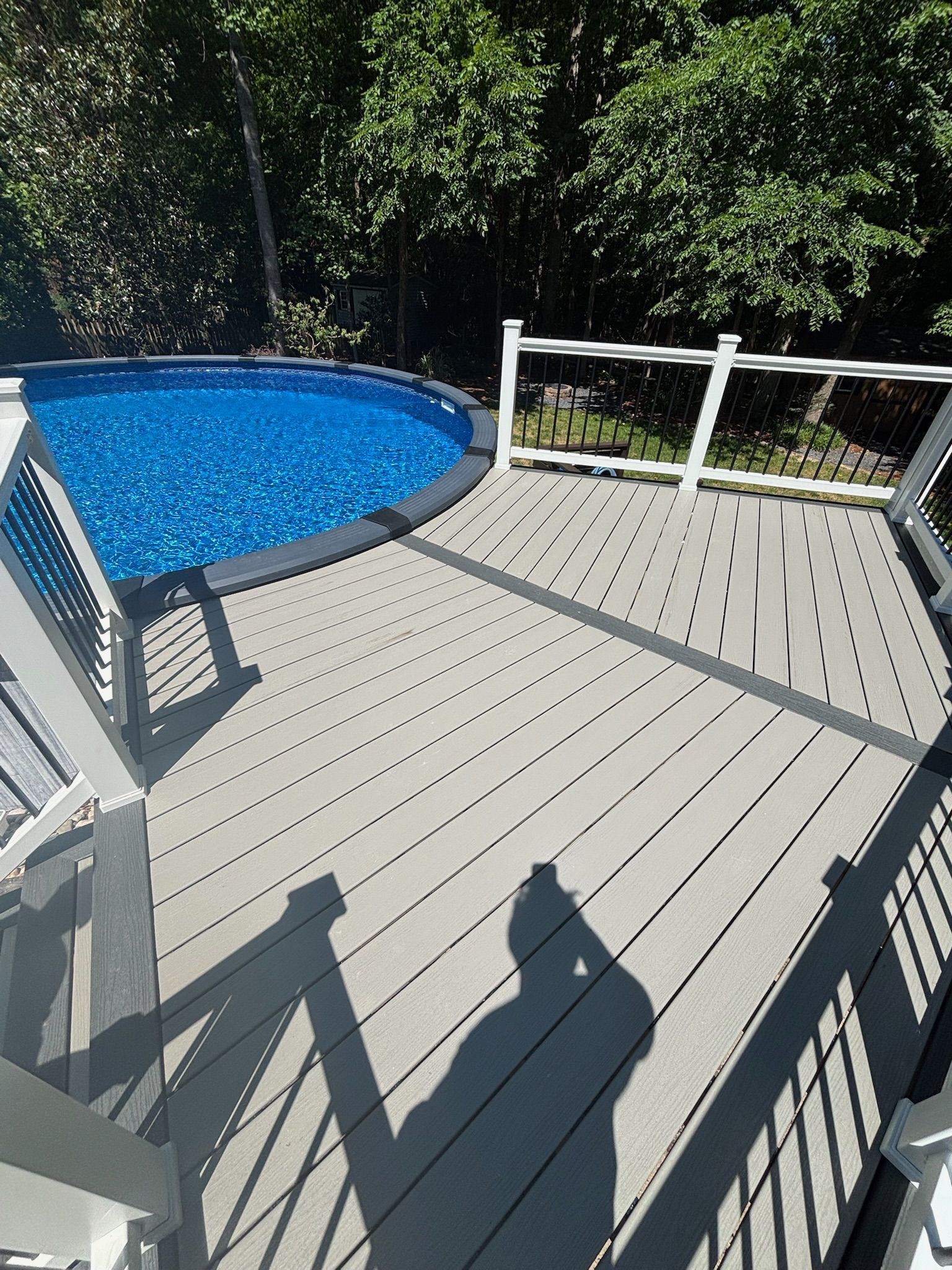 Backyard deck with a blue above-ground pool and white railing in bright sunlight