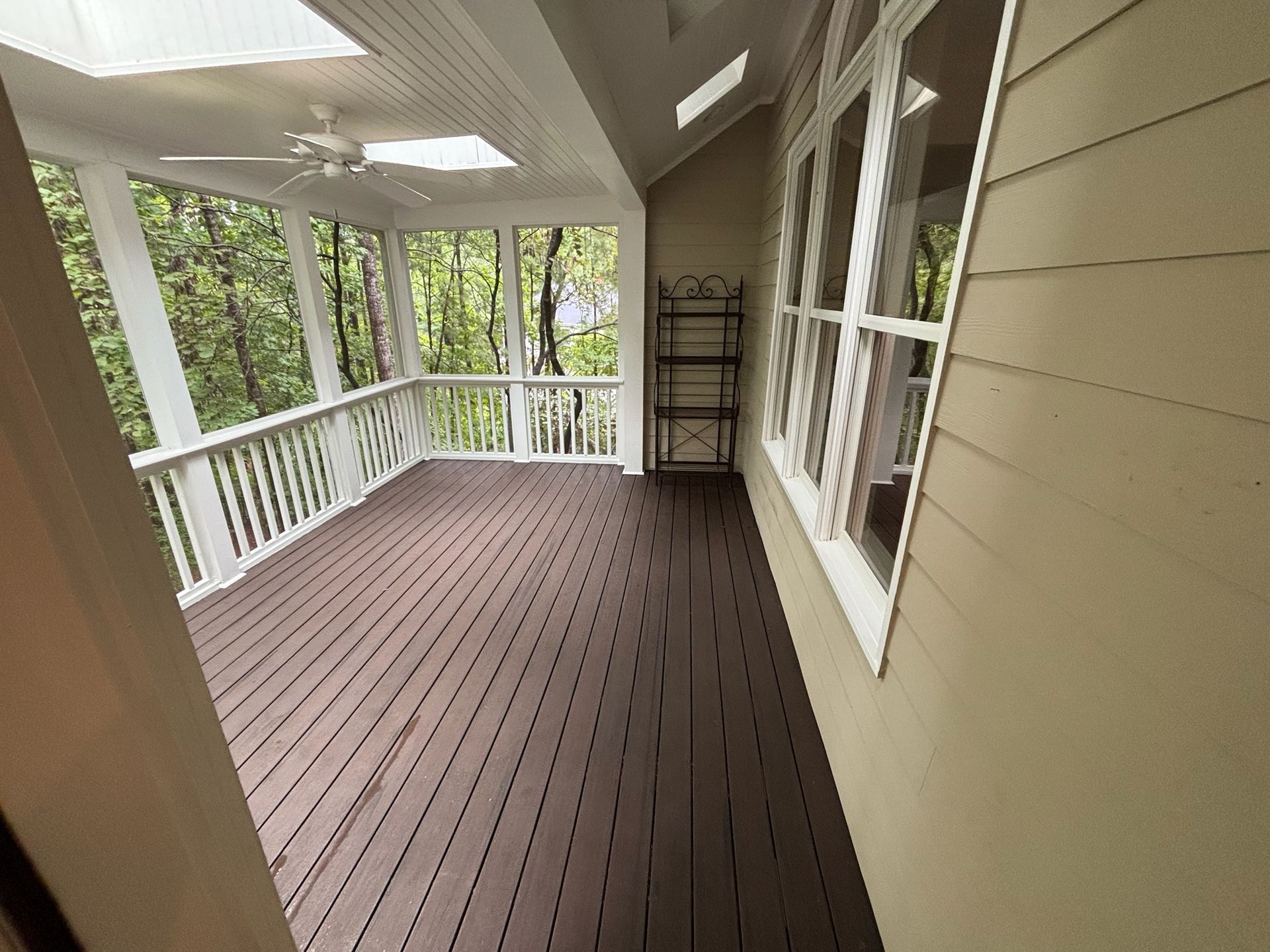 Covered porch with brown floorboards, white railing, windows, and a ladder against the wall.