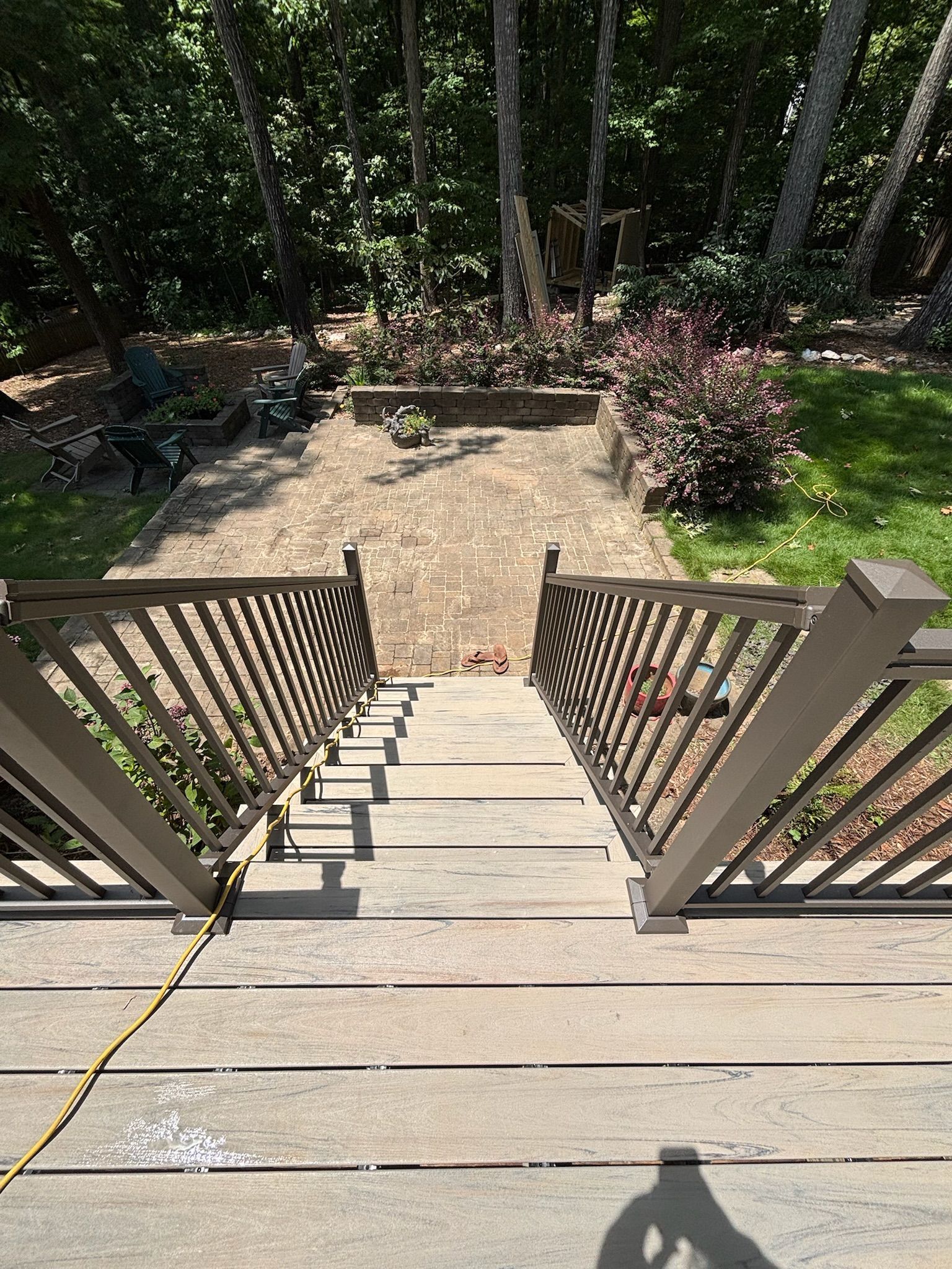 Wooden deck steps leading down to a sunlit garden with stone patio and trees